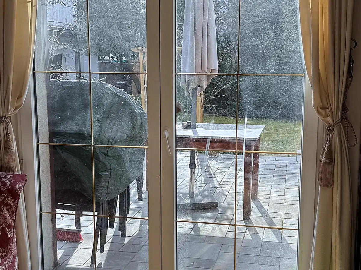 Drzwi tarasowe przed myciem — zamglona szyba z osadem, widok na ogród bez ostrości